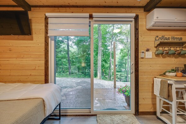 A wooden cabin room with a bed, a sliding glass door to a gravel area, and a coffee-themed wall decoration.