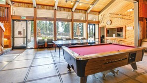 Ein Billardtisch in einem Raum mit Holzbalken, großen Fenstern und einem Deckenventilator.