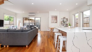 A modern kitchen with a marble countertop, a grey sofa, and a dining area with white chairs. - Casa Blue in Dromana (Dromana)