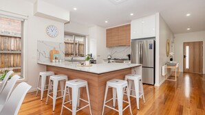 A modern kitchen with a central island, bar stools, a stainless steel refrigerator, and a clock on the wall. - Casa Blue in Dromana (Dromana)