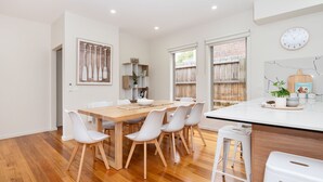 A modern kitchen with a wooden dining table, white chairs, and a white countertop with bar tools. - Casa Blue in Dromana (Dromana)