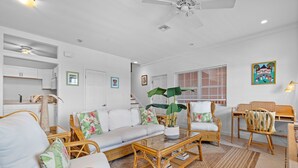 A living room with a white sofa, wicker chairs, a glass coffee table, and a dining area with wicker chairs and a table. - Convenient Stay in the Heart of Sandyport Olde Towne (Nassau)