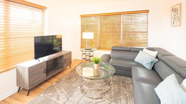 A living room with a sofa, TV, and a glass coffee table. - Modern 5 Bedroom Miami Home, 15 Min. to the Beach! (Miami)
