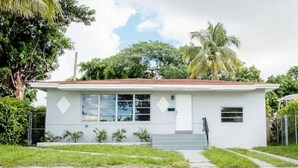 A single-story building with a flat roof, a front entrance with steps, and a small porch area with potted plants. - Modern 5 Bedroom Miami Home, 15 Min. to the Beach! (Miami)