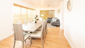 A modern living room with a dining area, featuring a wooden floor, a grey sofa, and a dining table with chairs. - Modern 5 Bedroom Miami Home, 15 Min. to the Beach! (Miami)
