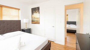 A hotel room with a large bed, a bedside table with a lamp, a door leading to another room, and a painting on the wall. - Modern 5 Bedroom Miami Home, 15 Min. to the Beach! (Miami)