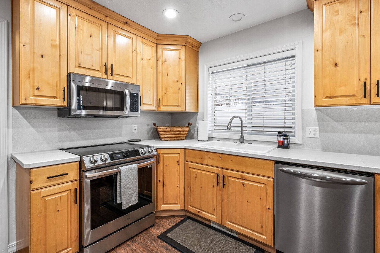 A modern kitchen with wooden cabinets, stainless steel appliances, and a window with blinds.