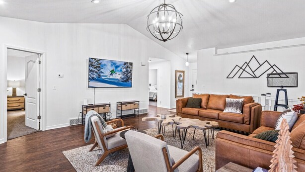 A spacious living room with a brown leather sofa, a coffee table, and a chandelier. There is a painting on the wall and a wooden sculpture on the coffee table.