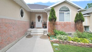 A two-story house with a front porch, a brick facade, and a small garden with potted plants.