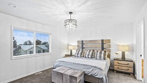 A bedroom with a large bed, a chandelier, a window with a view, and a nightstand with a lamp.