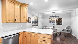 A modern kitchen with wooden cabinets, a stainless steel dishwasher, and a dining area with a table and chairs.
