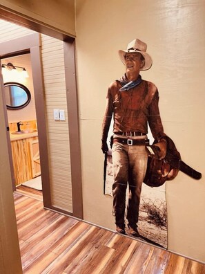 A corridor with a wooden floor and a wall with a large poster of a cowboy. - Texas Blue Apple | Pet-Friendly & Near Apple Store (Medina)