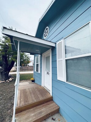A blue house with a wooden deck and a covered porch. - Texas Blue Apple | Pet-Friendly & Near Apple Store (Medina)