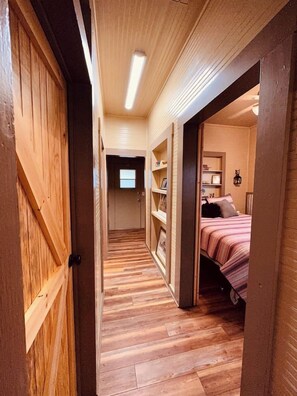 A narrow hallway with wooden flooring leading to a bedroom with a bed and a nightstand. - Texas Blue Apple | Pet-Friendly & Near Apple Store (Medina)