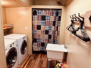 A compact laundry room with two front-loading washers, a white sink, a patchwork shower curtain, and a wall-mounted drying rack.