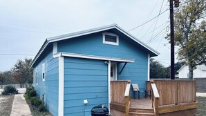 Una casa a un piano di colore blu con una veranda in legno e un barbecue di fronte.