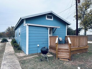 A blue single-story house with a wooden deck and a barbecue grill in front. - Texas Blue Apple | Pet-Friendly & Near Apple Store (Medina)