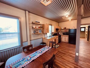 A compact kitchen with wooden cabinets, a dining table with a quilt, and a window providing natural light. - Texas Blue Apple | Pet-Friendly & Near Apple Store (Medina)