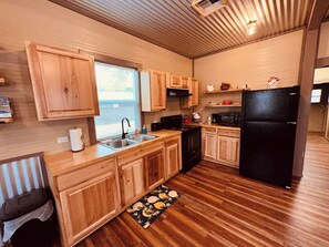 A compact kitchen with wooden cabinets, a black refrigerator, and a window providing natural light. - Texas Blue Apple | Pet-Friendly & Near Apple Store (Medina)