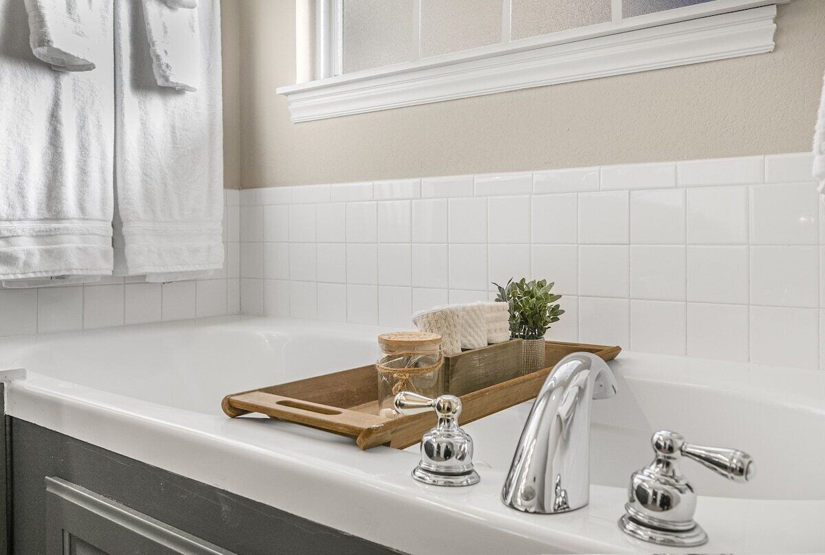 A bathroom with a white bathtub, a wooden tray with toiletries, and a window above the sink.