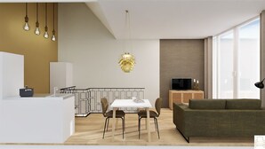A modern living room with a sofa, a dining area with a table and chairs, a kitchen with a white countertop and cabinets, and a large window providing natural light. - Residence d' Ouwe Kercke (Terneuzen)