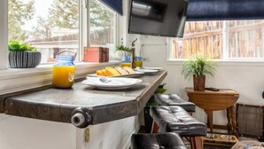 A kitchen with a built-in TV, wooden beams, a window with blinds, and a breakfast setup. - Ashore the Clouds | Glamping Awaits (Woodland Park)