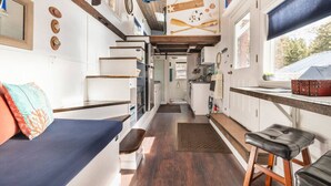 A compact kitchen with white cabinets, a wooden countertop, and a window with a view of trees. - Ashore the Clouds | Glamping Awaits (Woodland Park)
