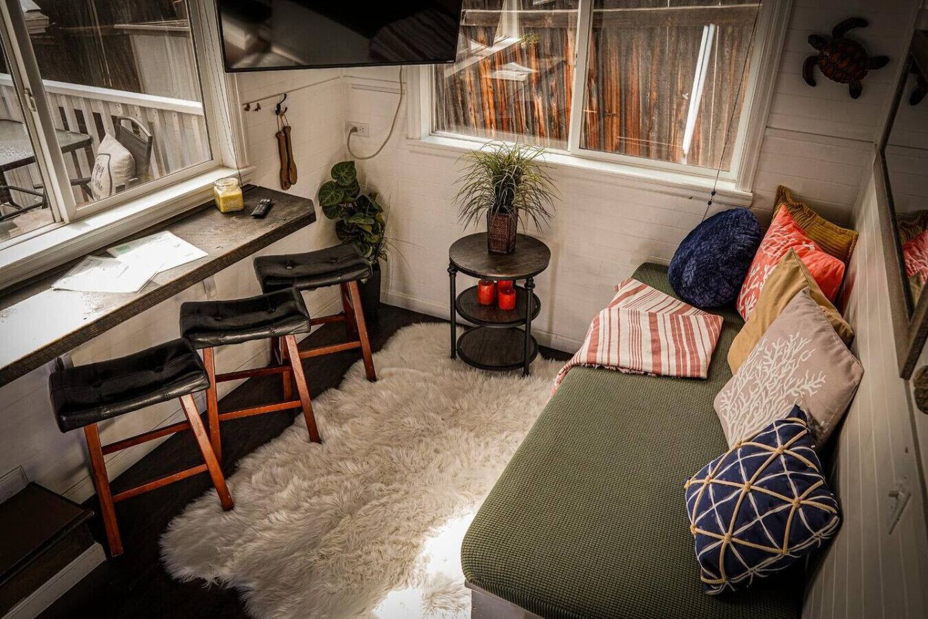 Une pièce chaleureuse comprenant un bureau, deux chaises, une petite table avec des bougies, un canapé agrémenté de coussins à motifs et une plante en pot.