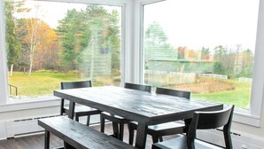 A dining area with a large table and chairs, large windows offering a view of a grassy yard and trees. - Mountainside Estate. Private Indoor Pool, near Ragged Mtn. & Sunapee, sleeps 28 (Wilmot)