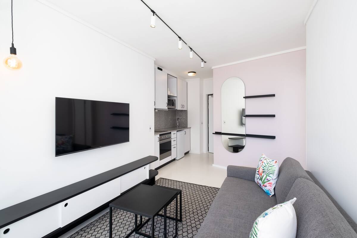 A modern living room with a flat-screen TV, a grey sofa, and a small black table.