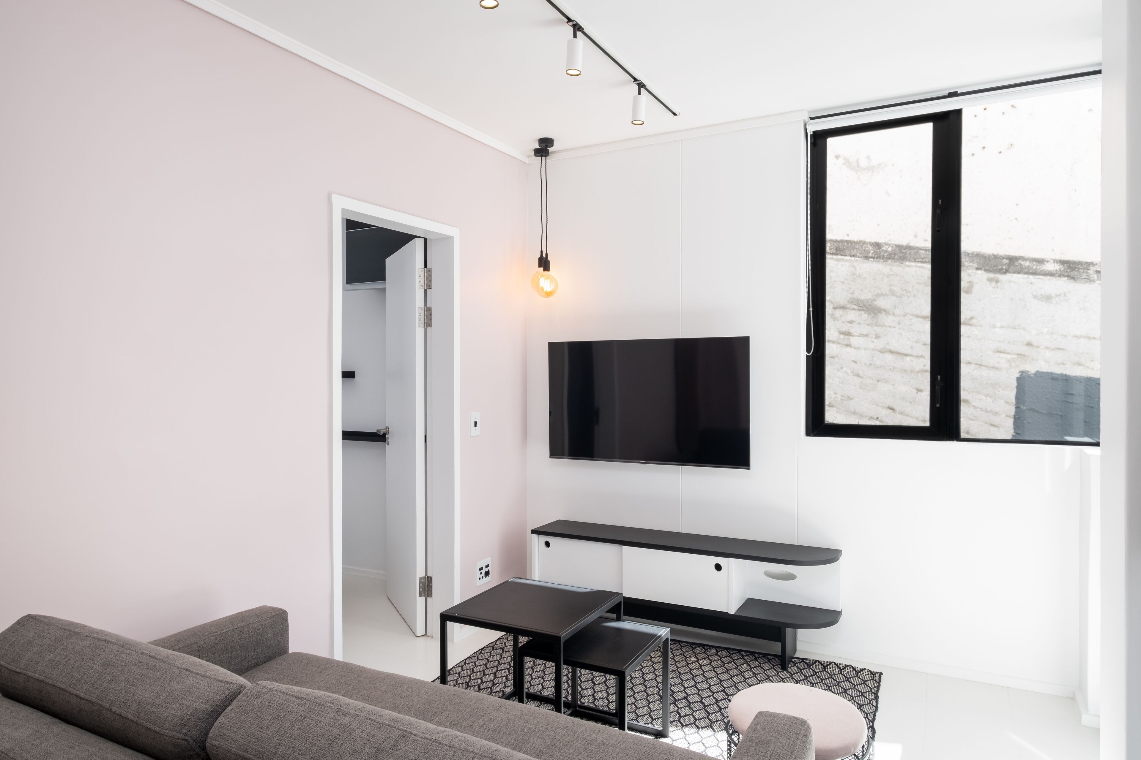 A modern living room with a sofa, a coffee table, a TV mounted on the wall, and a window providing a view of the outside.