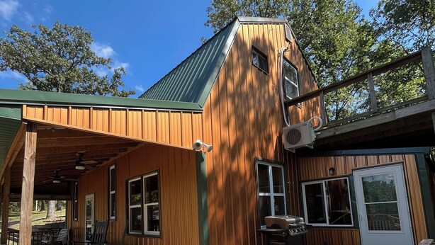 A wooden cabin with a covered porch, outdoor seating, and a view of the surrounding trees.