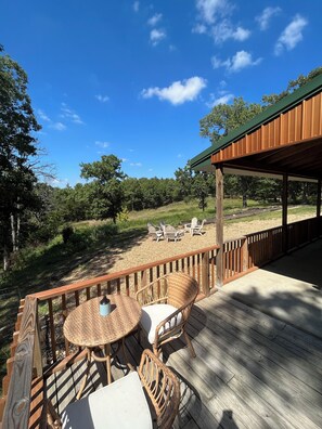 A wooden deck with wicker furniture and a covered area overlooking a gravel area with chairs.