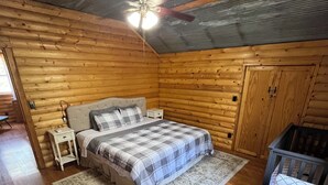 A cozy log cabin bedroom with a bed, nightstand, dresser, and a crib.