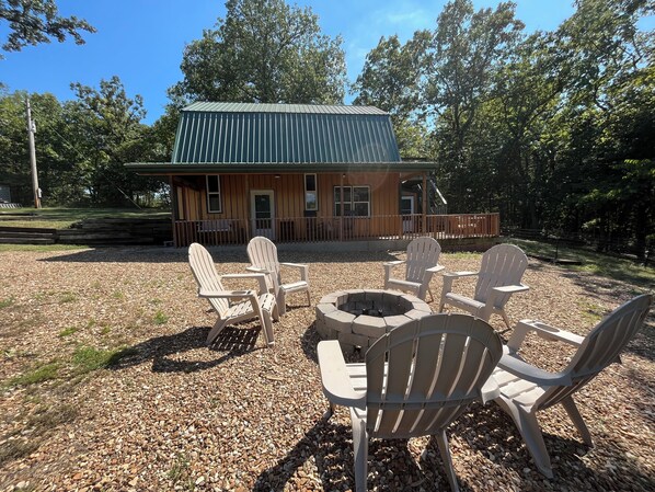 A lodge with a green roof, wooden exterior, and a deck with Adirondack chairs and a fire pit.