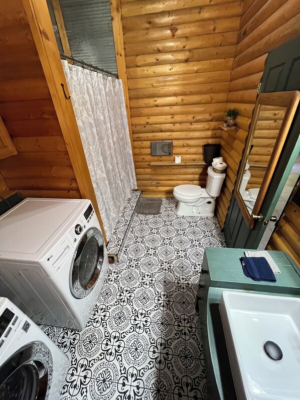 Un baño de cabaña de madera pequeño con lavadora, inodoro y lavamanos.