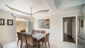 A dining area with a chandelier, a painting, and a modern kitchen with a stainless steel refrigerator. - 918 - Casa grande 3 Quartos 8 pessoas (Bombinhas)