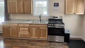 A kitchen with wooden cabinets, a stainless steel sink, a stove, and a trash can. - Riverview home (Pittsburg)