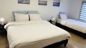 A bedroom with two beds, each with white bedding and light blue pillows. There are three wall-mounted paintings depicting seascapes.