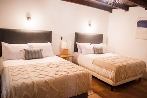 Two beds with headboards, a nightstand with a lamp, and a chandelier. - Mestizo Antigua (Antigua Guatemala)