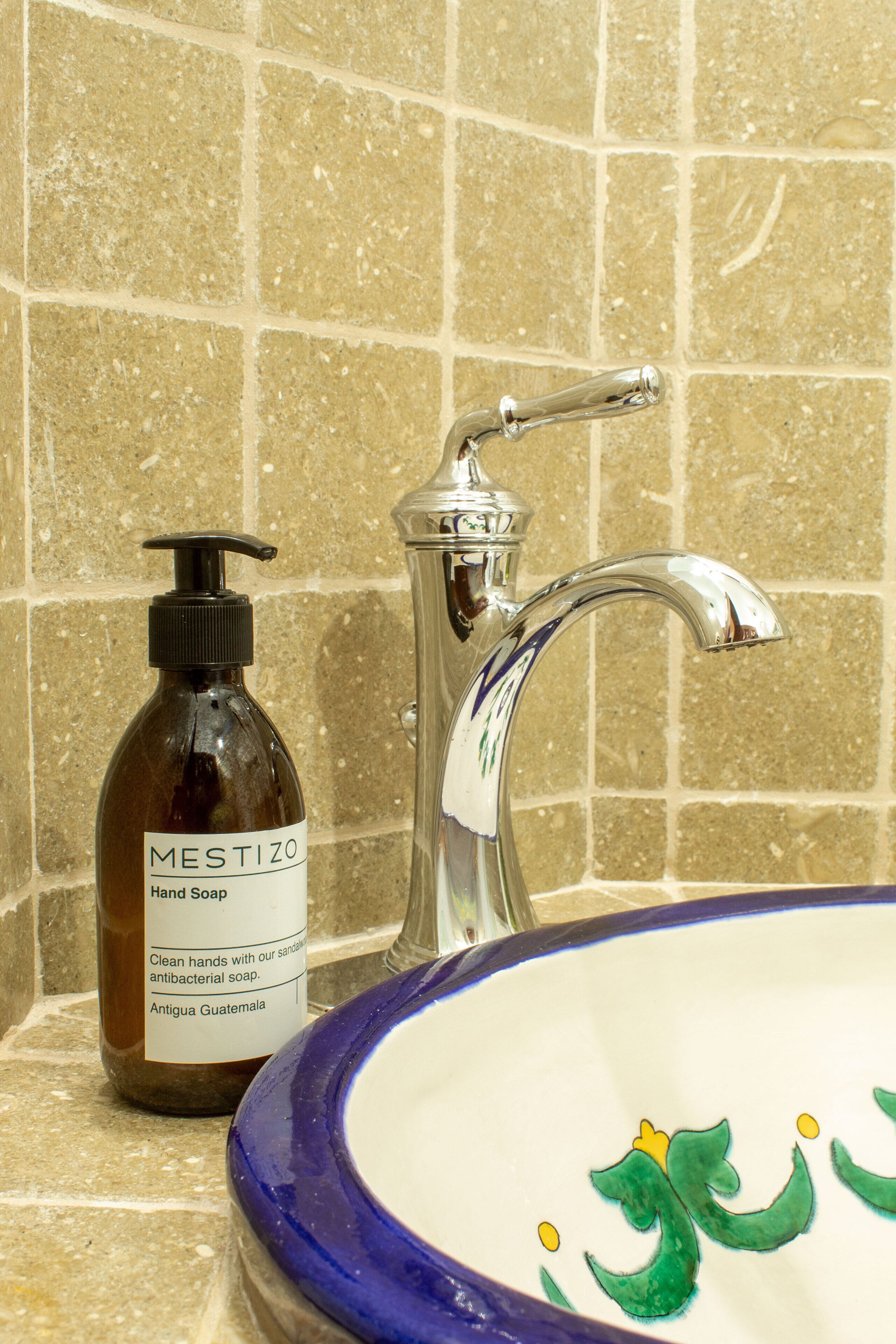 A bathroom with a hand soap bottle labeled 'MESTIZO' and a sink with a decorative blue rim.