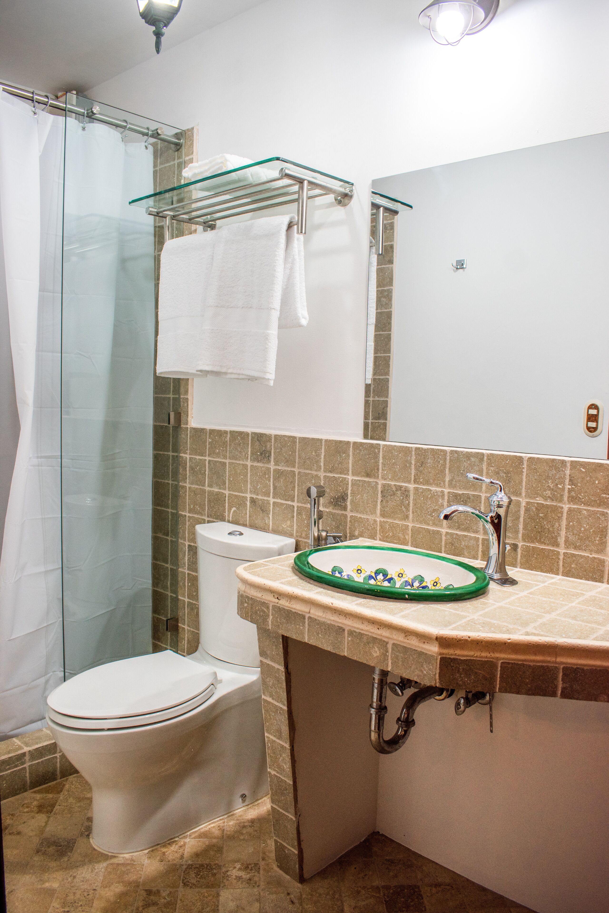 A bathroom with a glass shower enclosure, a white toilet, a sink with a green rim, and a towel rack.