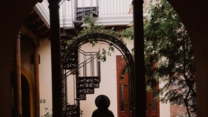 A person walking through an arched doorway with a staircase and a red door in the background. - Mestizo Antigua (Antigua Guatemala)