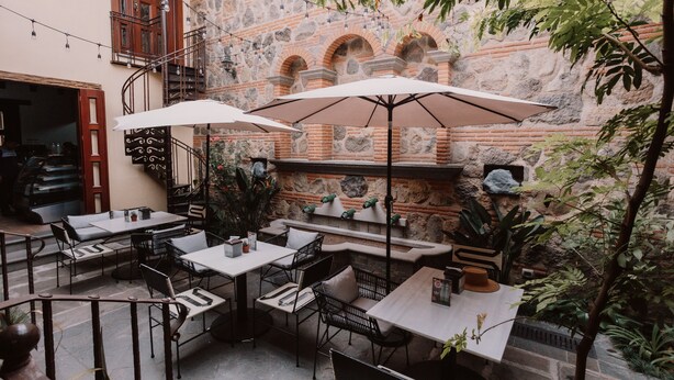 An outdoor patio with tables and chairs, stone walls, and string lights. - Mestizo Antigua (Antigua Guatemala)