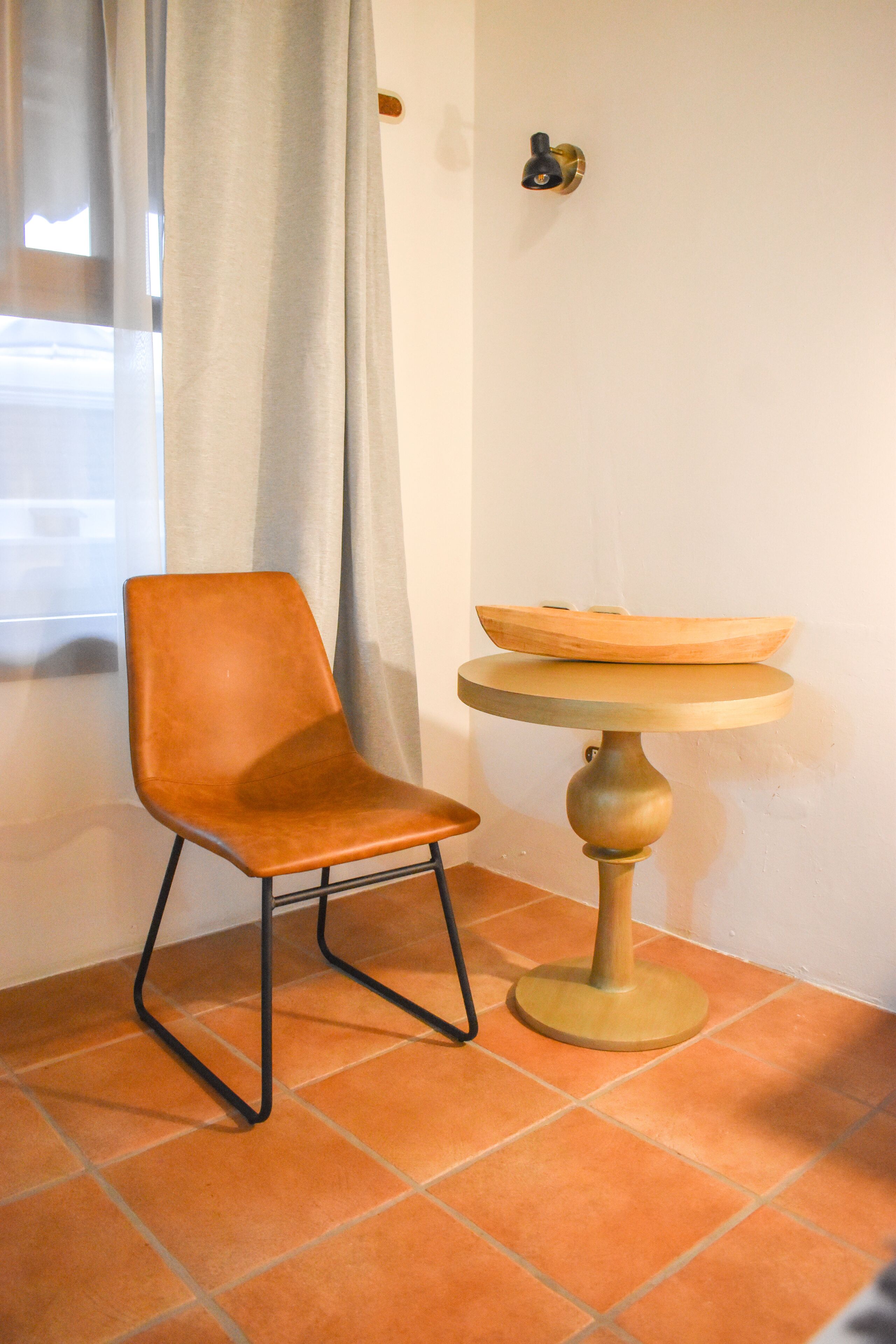 A chair and a small table with a bowl on top, positioned near a window with curtains.