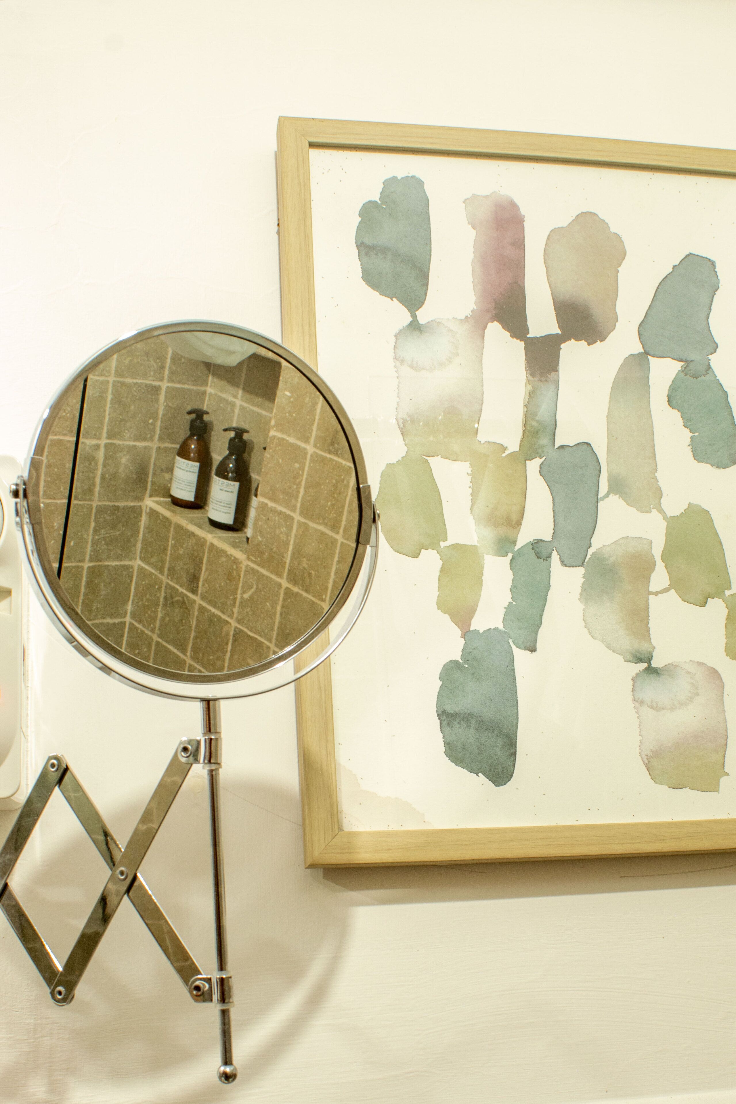 Um banheiro com espelho redondo, duas garrafas de shampoo e um quadro abstrato na parede.