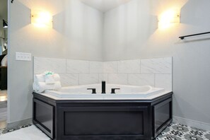 Une salle de bain d’angle avec une baignoire sur pieds, des carreaux de marbre blanc et deux appliques murales.