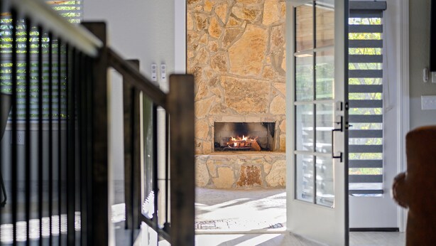 A stone fireplace with a fire, a staircase, and a door with blinds. - Romantic honeymoon cabin with hot tub! (Broken Bow)