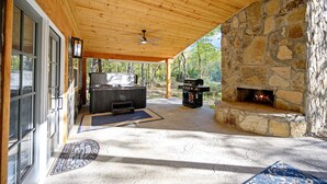 A covered outdoor area with a stone fireplace, a grill, and a seating area. - Romantic honeymoon cabin with hot tub! (Broken Bow)