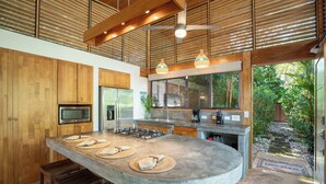 A modern kitchen with wooden cabinets, a large island, and a view of the garden. - Tropical Modern Home w/pool near the beach & surf (Nosara)